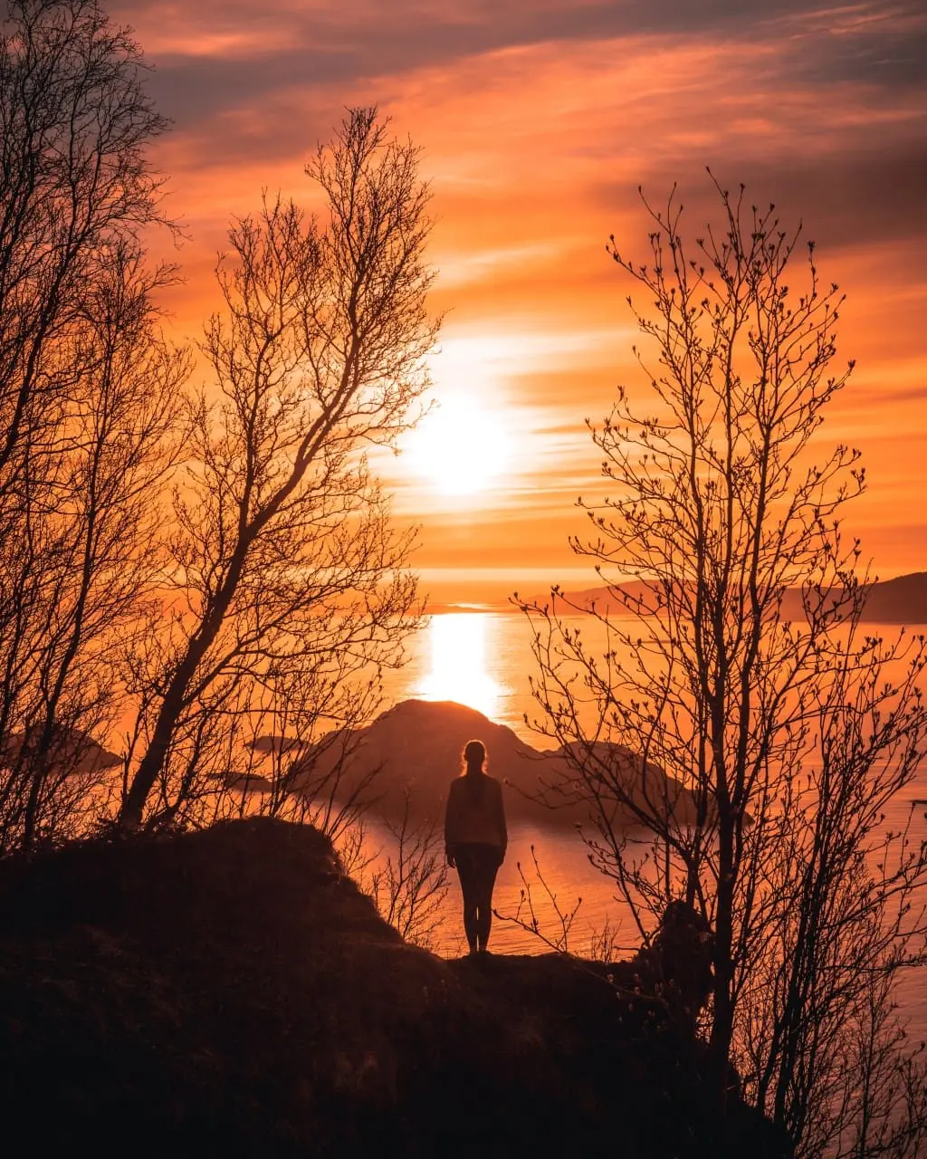 a woman standing on the edge of a cliff at sunset