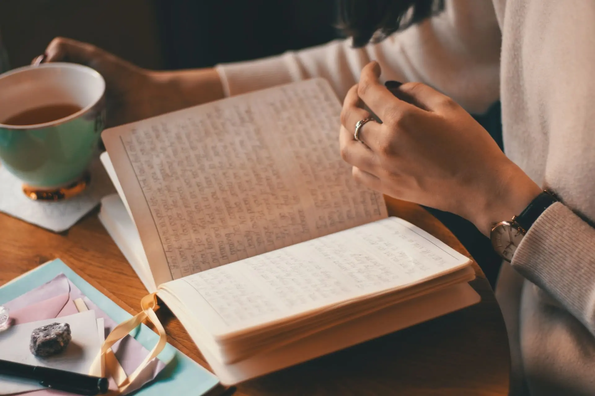 photo of a woman holding a cup and reading a journal